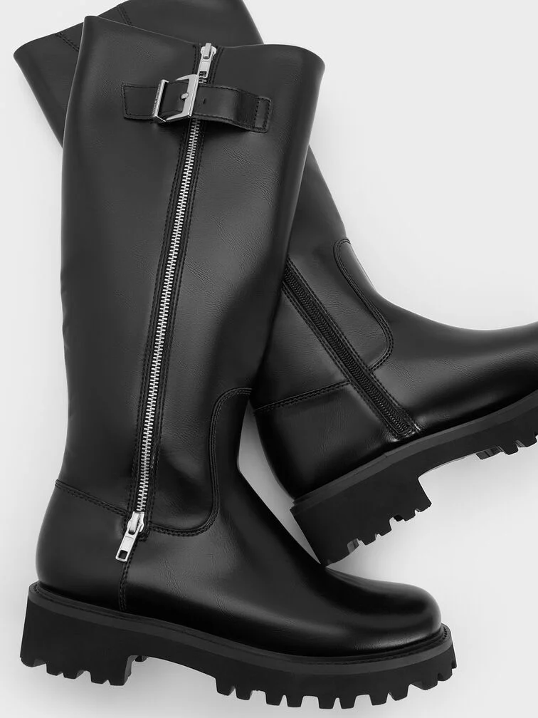 Black knee-high boots with a chunky lug sole, round toe and buckled zip detail at the shaft.