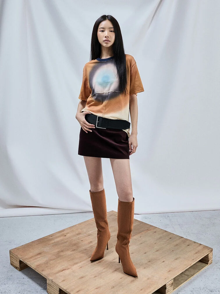 Cognac stiletto knee-high boots styled with a mini skirt and printed T-shirt.