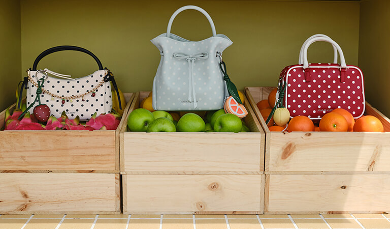 Hazel Polka-Dot Bow Top Handle Bag in cream with Strawberry Charm; Hazel Polka-Dot Bow Bucket Bag in sea-salt blue with Orange Slice Charm; Sianna Polka-Dot Bowling Bag in red with Lemon Charm - CHARLES & KEITH
