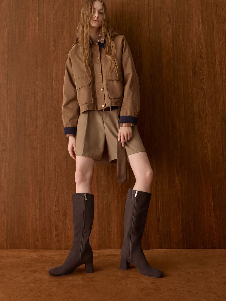 Dark brown square-toe knee-high boots paired with polished khaki tailored shorts.
